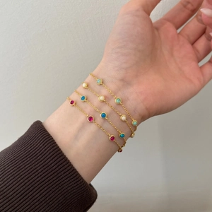 Detail of four gold bracelets featuring red, blue, green, and white round gemstones