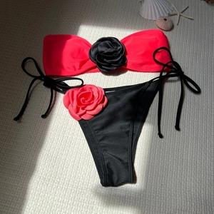 Detailed flat lay of pink bandeau bikini with black 3D rose and starfish beach props