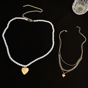 Detail of layered gold heart pendant chains and white pearl beaded necklace on black background