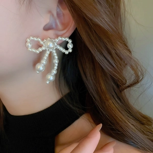 Close-up of elegant bow-shaped pearl drop earrings worn by a model in soft lighting