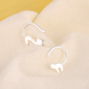 Asymmetric S925 sterling silver cat earrings with matte finish on beige fabric