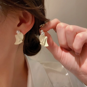 Détail d'une boucle d'oreille ondulée crème avec perle portée par un mannequin