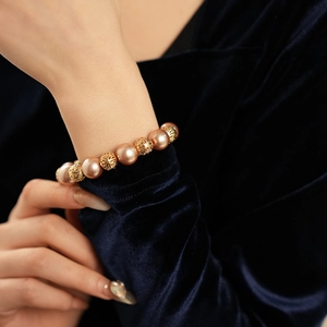 Detail of beaded bracelet with gold pearl-like beads and hollow patterns on wrist
