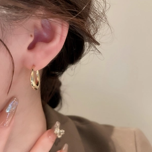Close-up of a woman wearing glossy gold U-shaped hoop earrings in a minimalist style