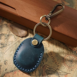 Close-up of dark blue leather AirTag case with bronze metal hook on vintage map