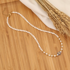 Detail of beaded necklace with white pearls, blue evil eye bead and gold lobster clasp