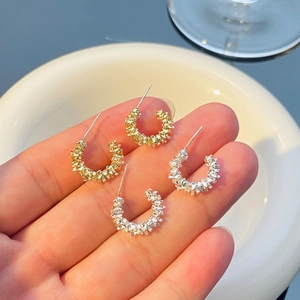 Detail of gold and silver textured C-shaped clip-on earrings held to show size
