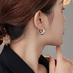 Detailed close-up of a silver U-shaped geometric hoop earring worn on a model's ear