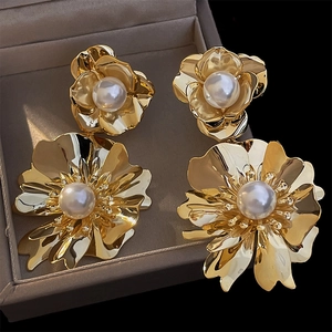 Détail de boucles d'oreilles fleur dorée avec perle dans un écrin à bijoux marron