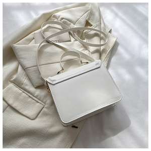 Detail view of white crossbody bag with metal buckle on beige blazer background