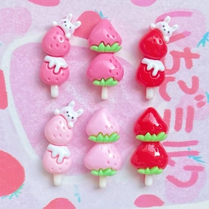 Flat lay of pink strawberry resin charms and ice cream accessories on a decorative paper