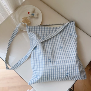 Detail of blue plaid canvas shoulder bag with embroidered bows on white background