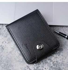 Short black textured leather wallet for men with secure snap closure on a stone surface