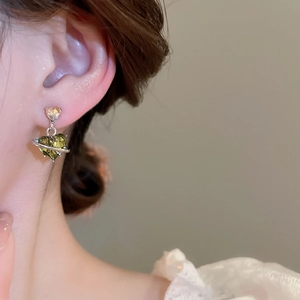 Macro shot of a heart-shaped green crystal earring with silver planet ring detail on model