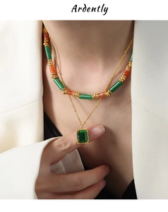 Dettaglio della collana a doppio strato con perline e ciondolo verde su blazer bianco