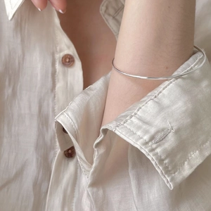 Close-up of a minimalist S925 sterling silver thin bangle on a linen shirt sleeve