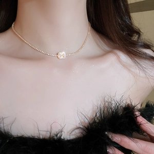 Close-up of luxury gold square zircon necklace worn by a model with feather accents