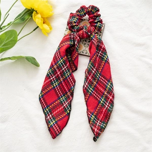 Close-up of red plaid velvet scrunchie with long ribbons on white fabric background