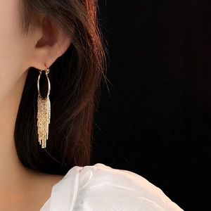 Boucles d'oreilles créoles dorées à pompons longs métalliques sur un mannequin asiatique