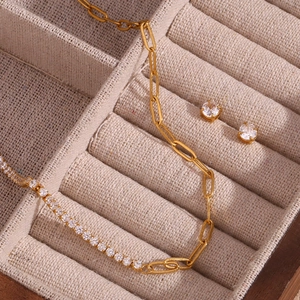 Macro shot of gold paperclip chain necklace and white zircon earrings in a beige velvet box
