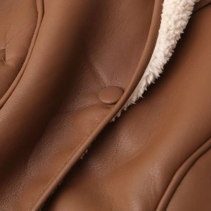 Détail d'une veste en cuir marron avec doublure en peau de mouton montrant le bouton en cuir