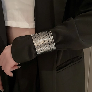 Close-up of layered silver hollow arm cuff worn over a black blazer sleeve for fashion styling