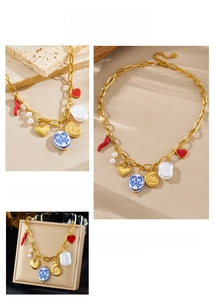 Detail of gold chain necklace with red chili, pearl, and floral heart pendants