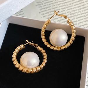 Macro detail of gold plated twisted metal hoop earrings with large lustrous white pearl