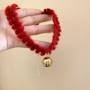 Gros plan du collier en tricot rouge avec clochette dorée et chaîne en métal réglable