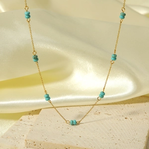 Close-up of a gold stainless steel necklace with blue turquoise beads on silk fabric