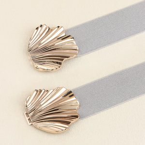 Details von grauen elastischen Gürteln mit goldenen Metall-Muschelschnallen auf Beige