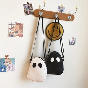 Detail of cartoon ghost-shaped PU leather crossbody bags hanging in a cozy indoor setting