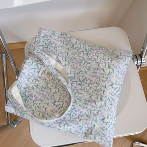 Détail du sac cabas en toile à fleurs avec imprimé floral mauve sur une chaise blanche