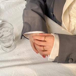 Detail of minimalist gold knot rings worn with elegant blazer for a layered jewelry look