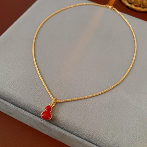 Detail of double-sided red gourd pendant on a gold-plated necklace displayed on velvet