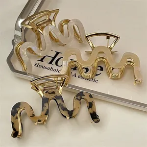 Three acetate wave hair claws in tortoiseshell and cream on a white ceramic tray