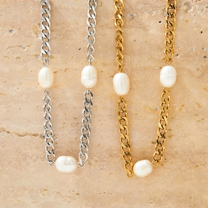 Golden and silver Cuban chain necklaces with irregular white pearls on a stone surface