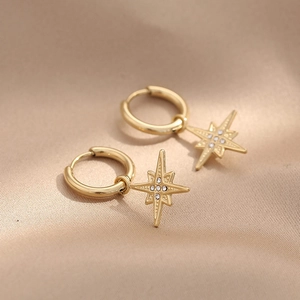 Elegant gold North Star hoop earrings with sparkling rhinestones on soft silk background