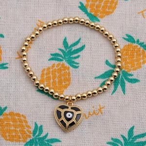 Close-up of gold beaded bracelet featuring a heart-shaped evil eye charm on fabric