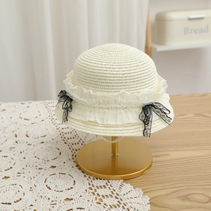 Détail d'un chapeau de paille crème avec bordure en dentelle blanche et nœuds noirs