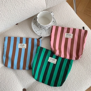 Three striped canvas makeup bags in blue, pink, and green arranged on a textured surface
