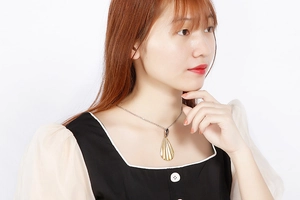 Detail of long golden teardrop pendant with vertical stripes on a simple necklace