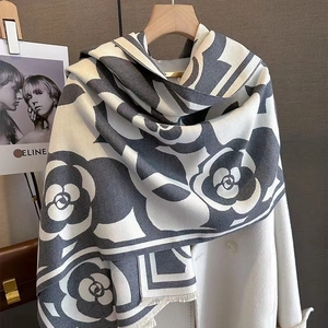 Detail of grey and white camellia pattern scarf with fringe, hanging on a white coat