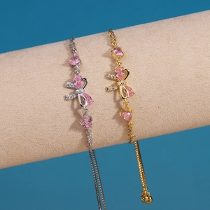 Detail of gold and silver bow bracelets with pink teardrop zircon on a velvet stand