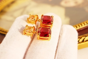 Detailed close-up of retro gold-plated drop earrings with red and yellow gemstones