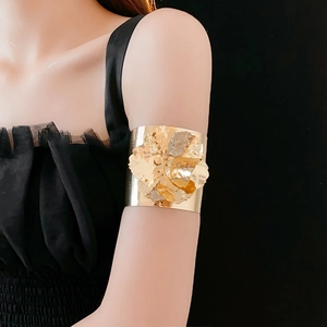 Artistic gold metal floral arm cuff worn by a model against a deep black background