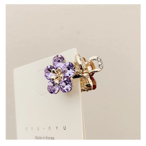 Detail of a mini gold-plated hair claw clip featuring purple crystal flower and rhinestones