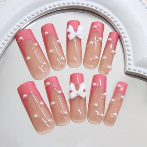 Pink French long ballerina press-on nails with white bows and pearls on a mirror