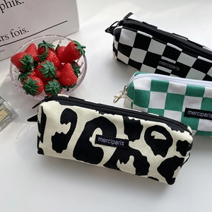 Three canvas pencil cases in checkerboard and leopard patterns with a bowl of strawberries