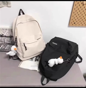 Dettaglio di zaini in tela con ciondoli a forma di anatra bianca nei colori nero e beige